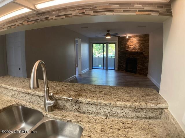 kitchen featuring sink, ceiling fan, dark hardwood / wood-style floors, light stone counters, and a fireplace