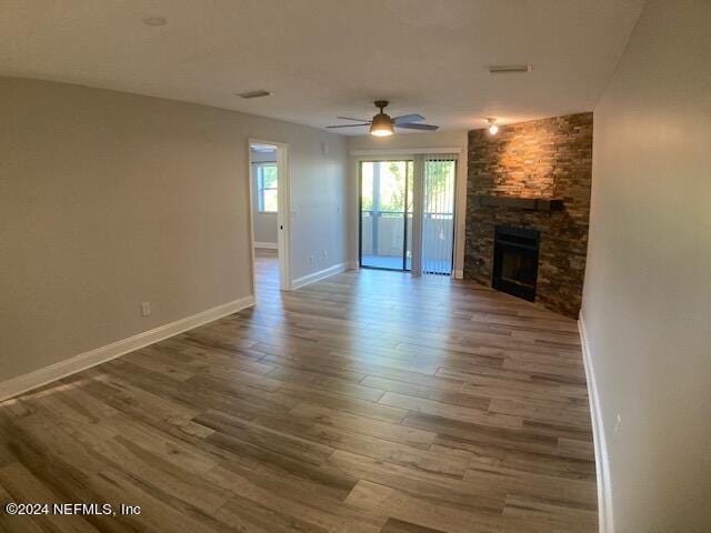 unfurnished living room featuring a stone fireplace, wood-type flooring, and ceiling fan