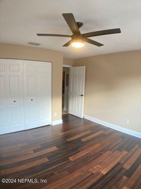 unfurnished bedroom featuring dark wood-type flooring, ceiling fan, and a closet