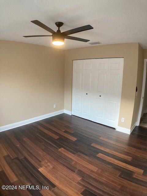 unfurnished bedroom with dark wood-type flooring, ceiling fan, and a closet