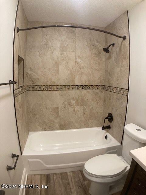 full bathroom featuring tiled shower / bath, hardwood / wood-style flooring, vanity, toilet, and a textured ceiling