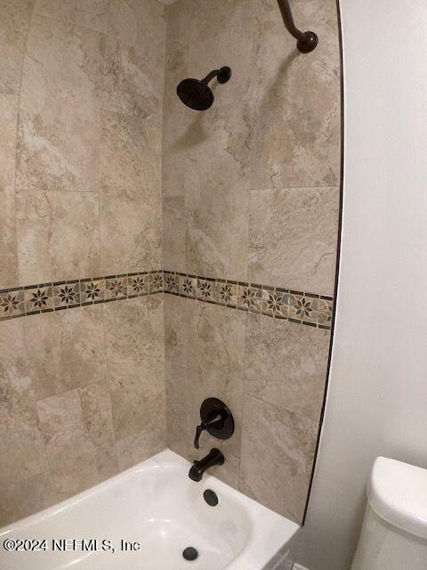 bathroom featuring tiled shower / bath combo and toilet