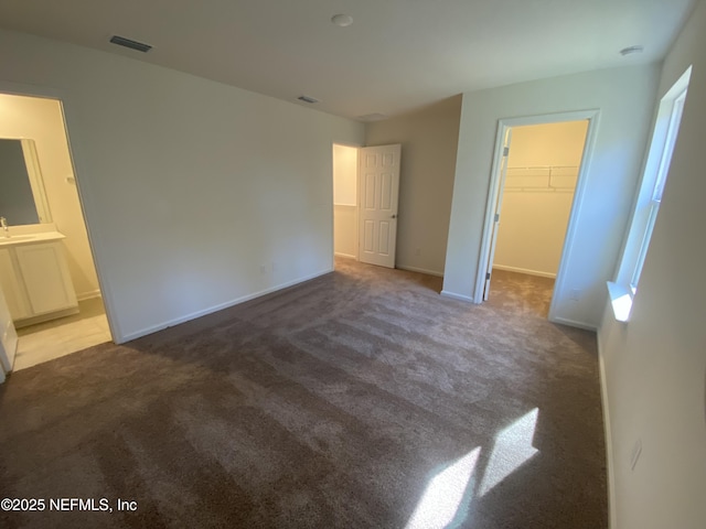 unfurnished bedroom featuring dark colored carpet, ensuite bathroom, a spacious closet, and a closet