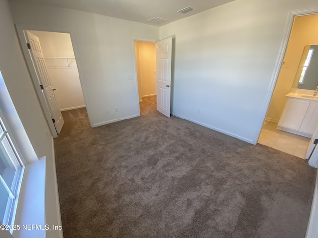 unfurnished bedroom with connected bathroom, sink, light colored carpet, a walk in closet, and a closet