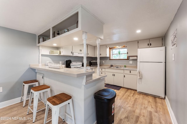 kitchen featuring a breakfast bar area, white appliances, kitchen peninsula, light hardwood / wood-style floors, and sink