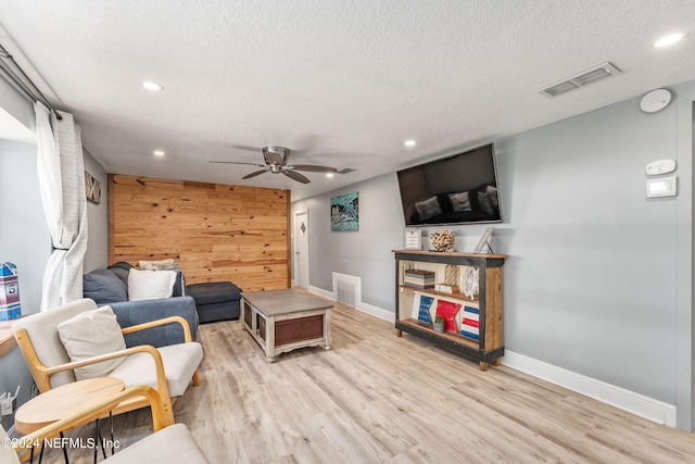 living room with wooden walls, a textured ceiling, ceiling fan, and light wood-type flooring