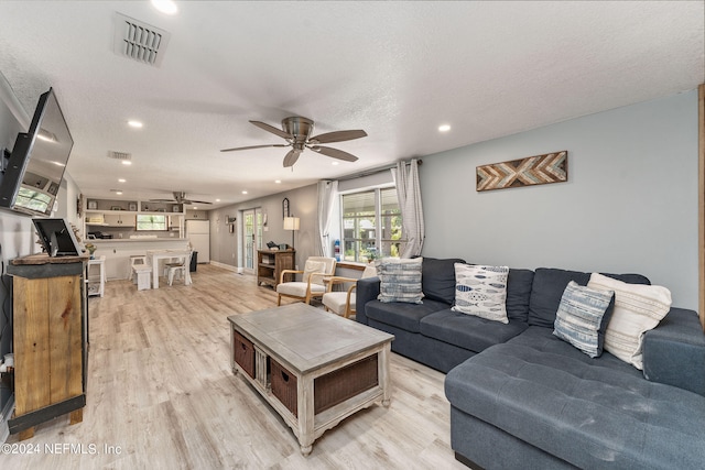 living room with light hardwood / wood-style flooring, a textured ceiling, and ceiling fan