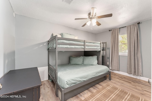 bedroom with a textured ceiling, ceiling fan, and light wood-type flooring