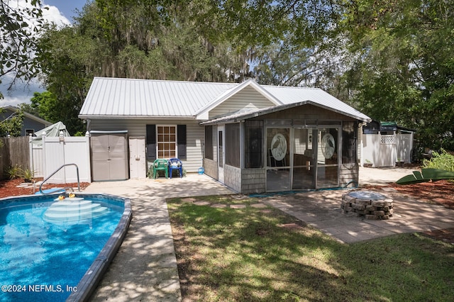 rear view of house featuring a fire pit, a sunroom, a fenced in pool, an outdoor structure, and a patio