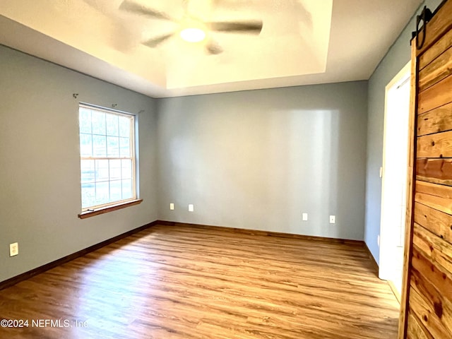 spare room with a raised ceiling, ceiling fan, a barn door, and light hardwood / wood-style floors