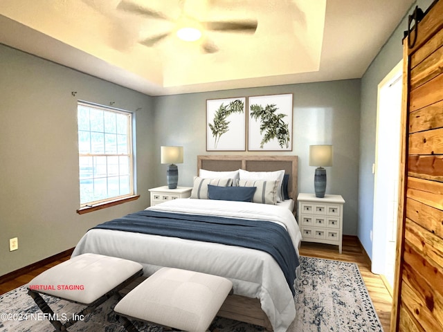 bedroom featuring ceiling fan, a barn door, a raised ceiling, and light wood-type flooring