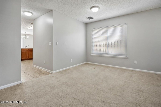 carpeted spare room with sink, a textured ceiling, and an inviting chandelier