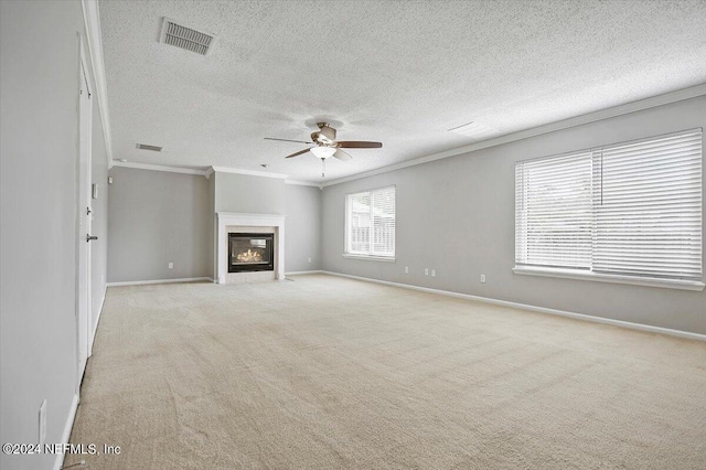 unfurnished living room featuring light colored carpet, ornamental molding, ceiling fan, and a textured ceiling