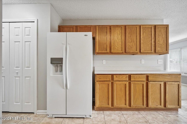 kitchen with white fridge with ice dispenser, light tile patterned floors, and a textured ceiling