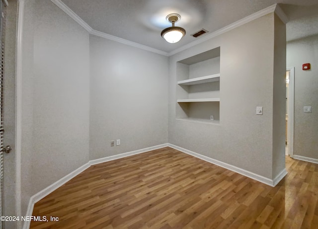 empty room featuring built in shelves, a textured ceiling, crown molding, and hardwood / wood-style floors