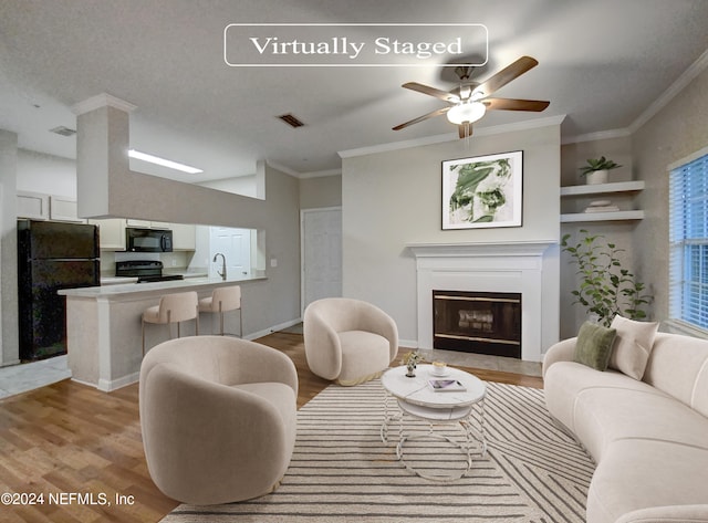 living room with a textured ceiling, ceiling fan, light hardwood / wood-style floors, sink, and ornamental molding