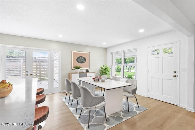 dining space with french doors, a healthy amount of sunlight, light hardwood / wood-style floors, and a textured ceiling