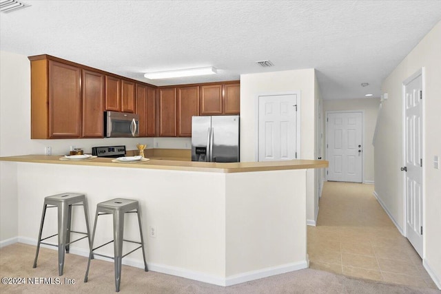 kitchen featuring a kitchen bar, kitchen peninsula, stainless steel appliances, light carpet, and a textured ceiling