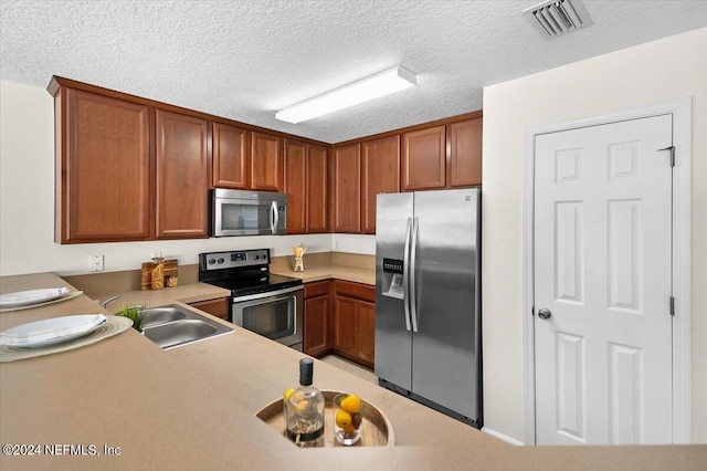 kitchen with sink, kitchen peninsula, a textured ceiling, and appliances with stainless steel finishes