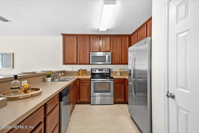 kitchen with appliances with stainless steel finishes, sink, light tile patterned floors, and a textured ceiling