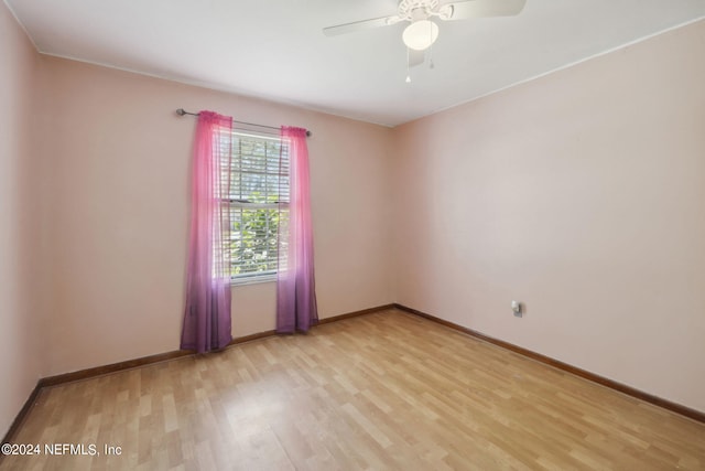 spare room featuring light wood finished floors, a ceiling fan, and baseboards