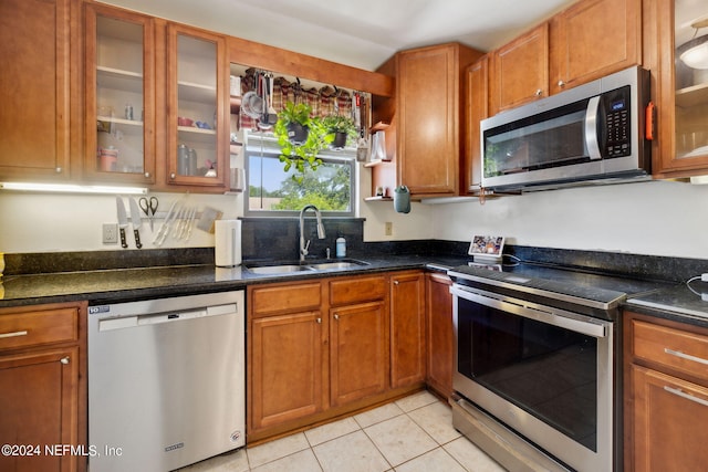 kitchen with brown cabinets, light tile patterned floors, stainless steel appliances, glass insert cabinets, and a sink