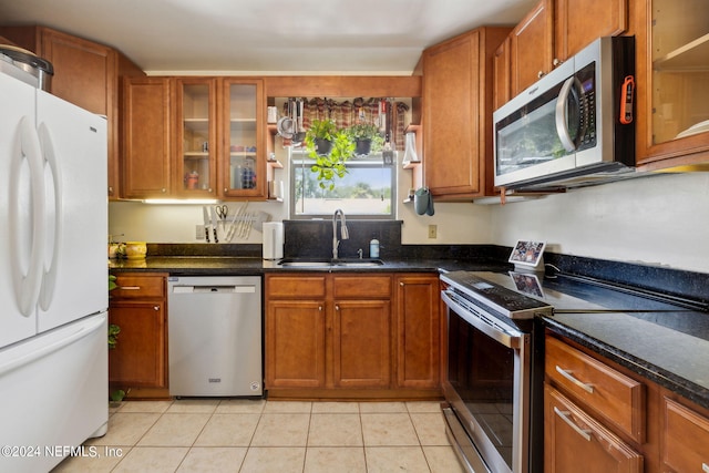 kitchen with dark stone countertops, sink, stainless steel appliances, and light tile patterned flooring