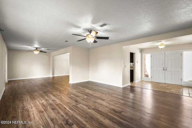 unfurnished living room featuring dark wood-type flooring, a textured ceiling, and ceiling fan