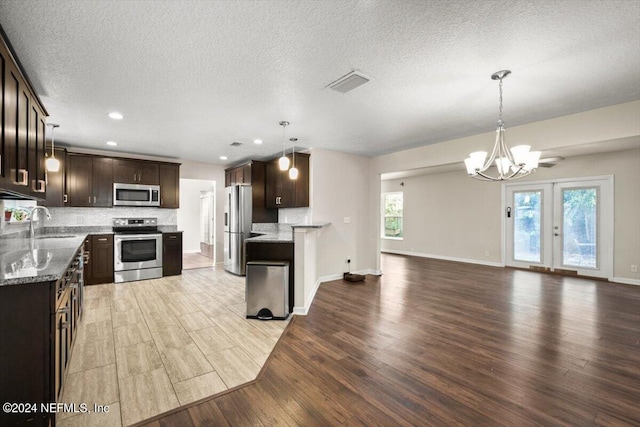 kitchen with tasteful backsplash, hanging light fixtures, dark brown cabinets, light wood-type flooring, and stainless steel appliances