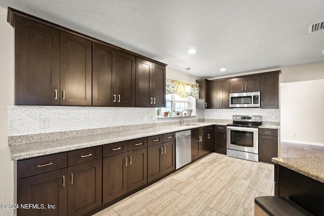 kitchen with light stone counters, dark brown cabinetry, appliances with stainless steel finishes, and sink