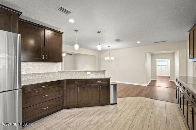 kitchen featuring pendant lighting, stainless steel fridge, backsplash, light stone counters, and dark brown cabinetry