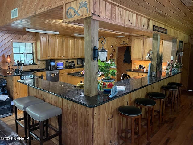 kitchen featuring dark stone countertops, wooden walls, dark hardwood / wood-style floors, and stainless steel dishwasher