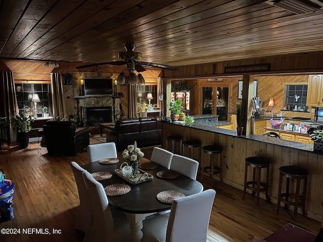 dining area featuring dark wood-type flooring, a fireplace, wooden ceiling, and wooden walls