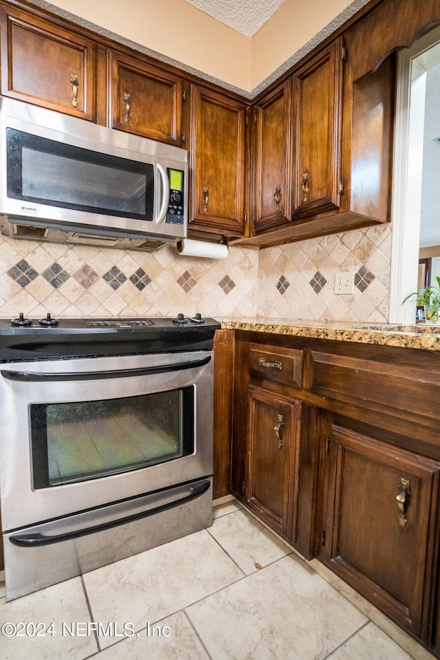 kitchen with range, light tile patterned flooring, light stone countertops, and decorative backsplash