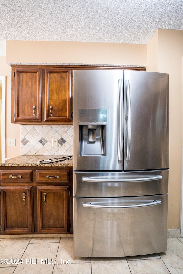 kitchen with stainless steel fridge, light tile patterned flooring, tasteful backsplash, and light stone counters