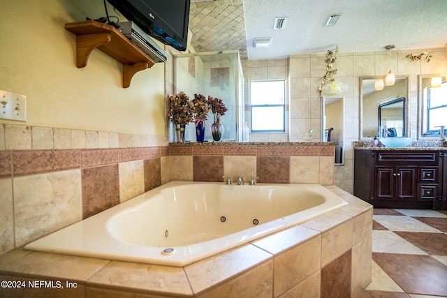 bathroom featuring tile patterned flooring, tiled tub, vanity, and a textured ceiling