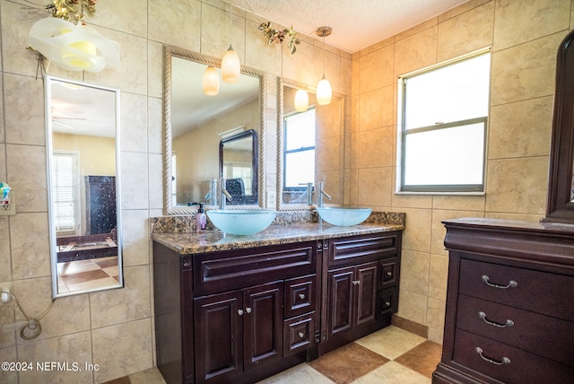 bathroom with dual vanity, tile patterned floors, a textured ceiling, and tile walls