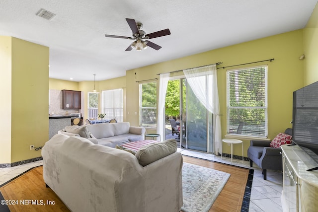 living room with ceiling fan, a textured ceiling, and light tile patterned flooring