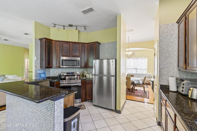 kitchen featuring light tile patterned flooring, appliances with stainless steel finishes, kitchen peninsula, and dark stone counters