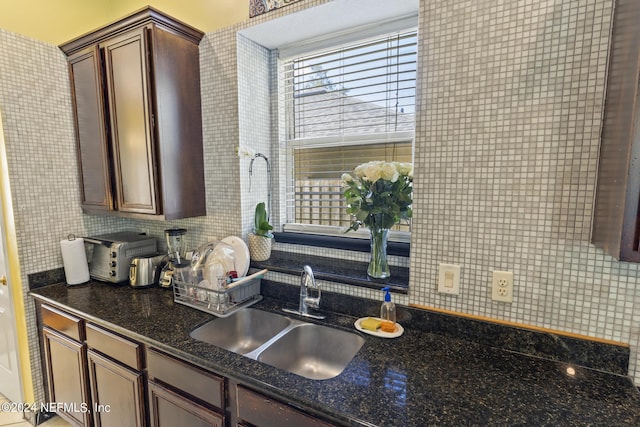 kitchen with decorative backsplash, sink, dark brown cabinets, and dark stone countertops