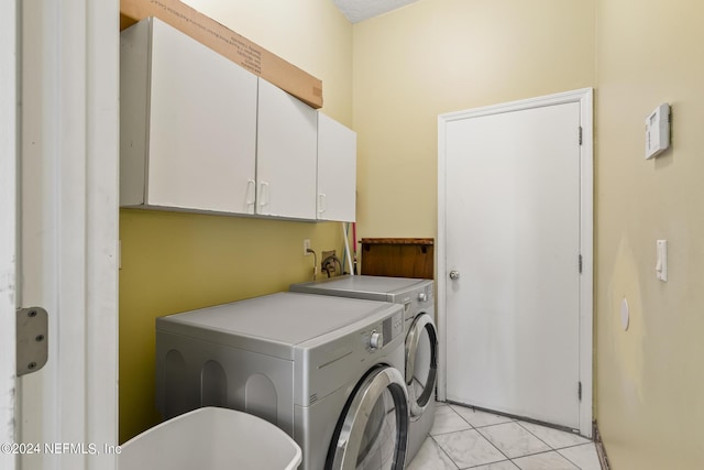 clothes washing area featuring light tile patterned floors, cabinets, and washing machine and clothes dryer