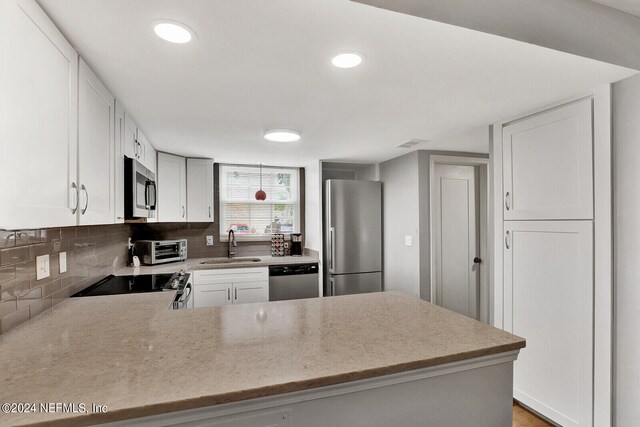 kitchen featuring backsplash, light stone counters, sink, kitchen peninsula, and stainless steel appliances