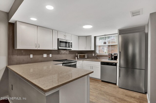 kitchen featuring backsplash, white cabinetry, appliances with stainless steel finishes, light stone countertops, and sink