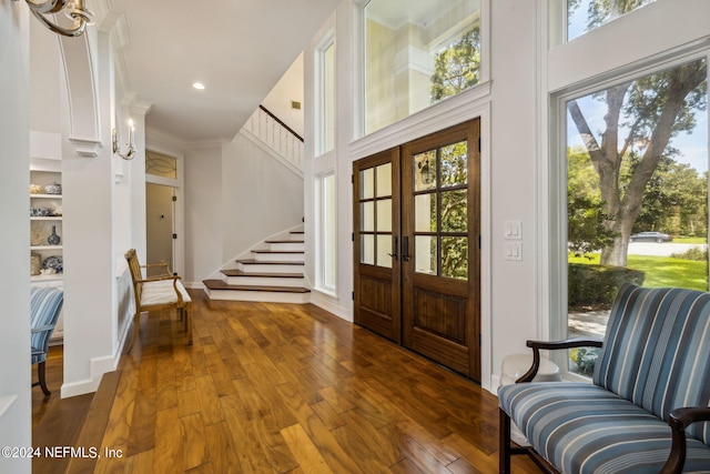 entrance foyer featuring a towering ceiling, dark wood-type flooring, ornamental molding, and french doors