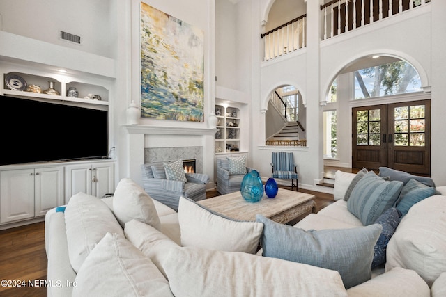 living room featuring built in shelves, dark hardwood / wood-style floors, french doors, and a high ceiling