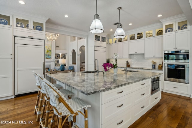 kitchen featuring white cabinetry, light stone countertops, a center island with sink, and paneled built in refrigerator