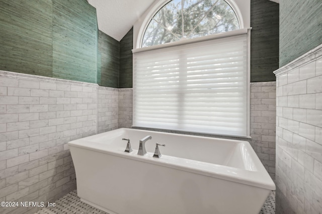 bathroom featuring vaulted ceiling, tile walls, a textured ceiling, and a tub to relax in