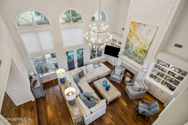 living room with dark wood-type flooring, built in shelves, a high ceiling, and a notable chandelier