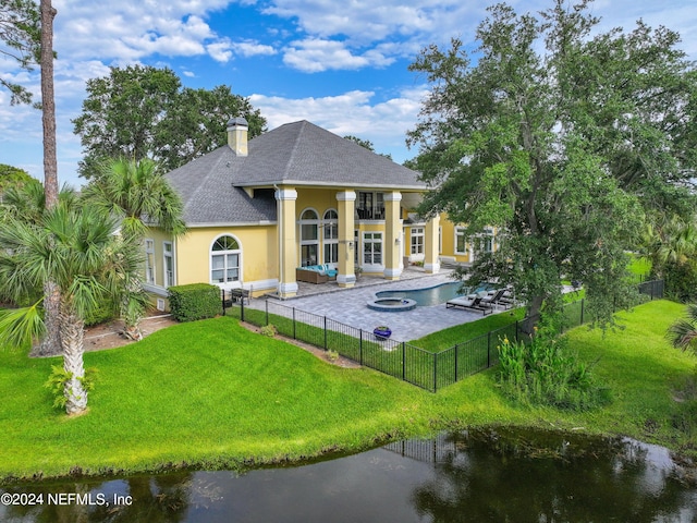 rear view of property with a water view, a balcony, a yard, and a swimming pool with hot tub