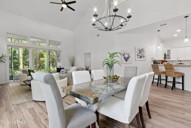 dining space featuring light hardwood / wood-style flooring, ceiling fan with notable chandelier, and high vaulted ceiling